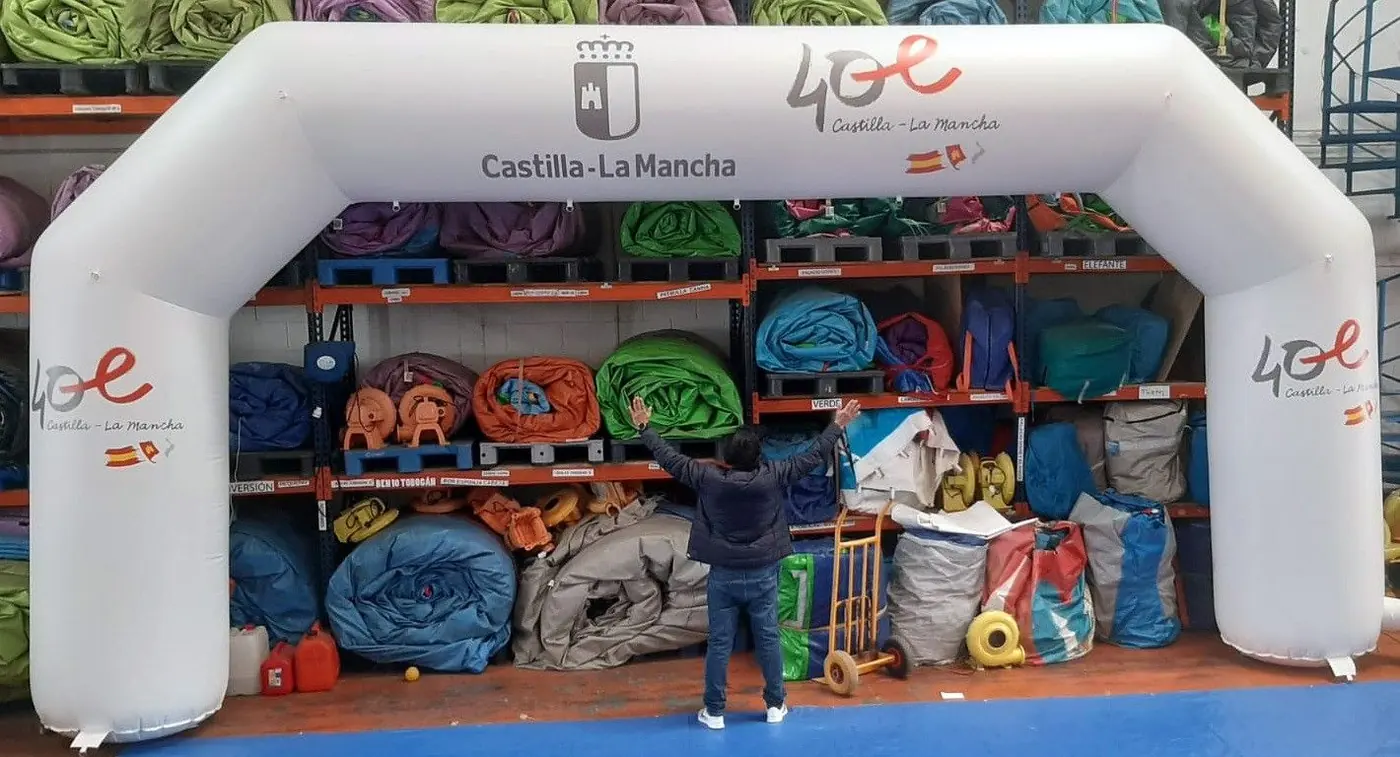Arco hinchable blanco con los logotipos de la Junta de Castilla-La Mancha, delante de rollos de material