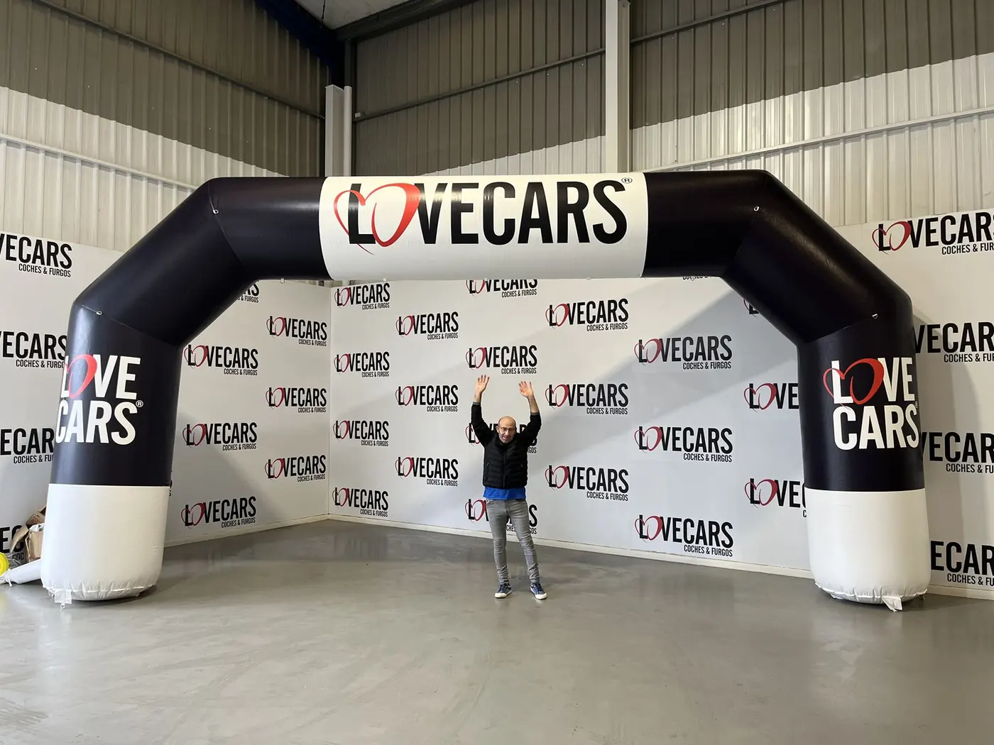 Arco hinchable negro y blanco de Love Cars, con una persona debajo para dar escala, delante del photocall de la marca