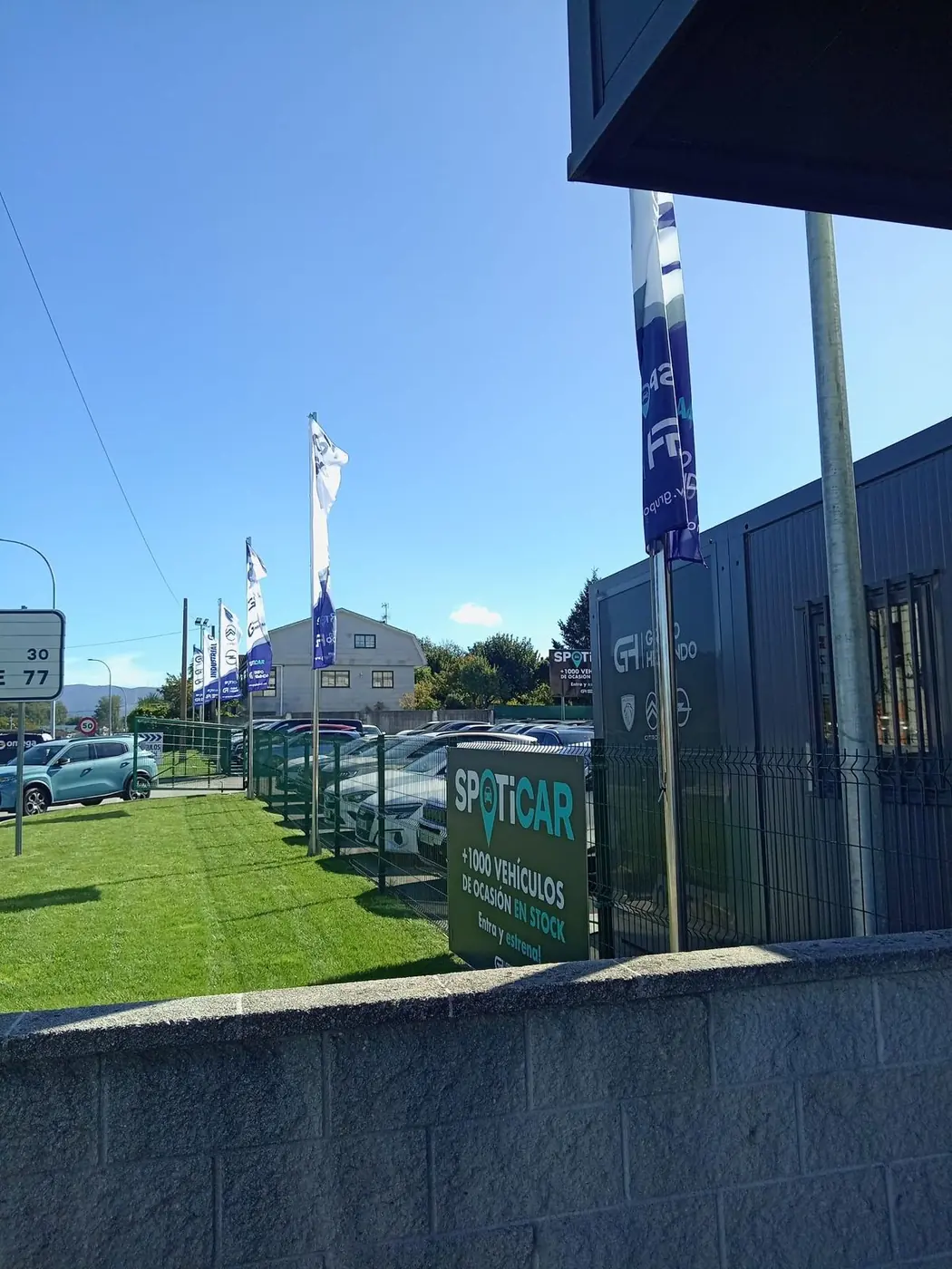 Banderas publicitarias azules y blancas sobre mástiles delante de un concesionario