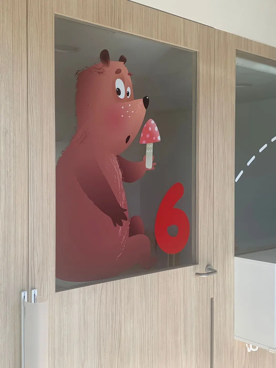 Vinilo de un oso rojo con el número 6 junto a la puerta de un aula