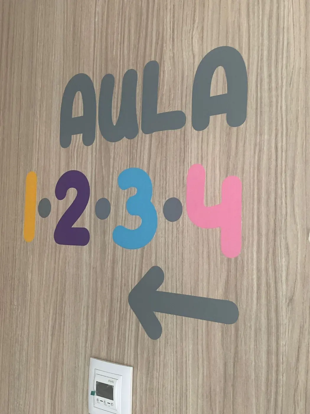 Rotulación Aula 1, 2, 3, 4 con una flecha, en colores sobre la pared de madera