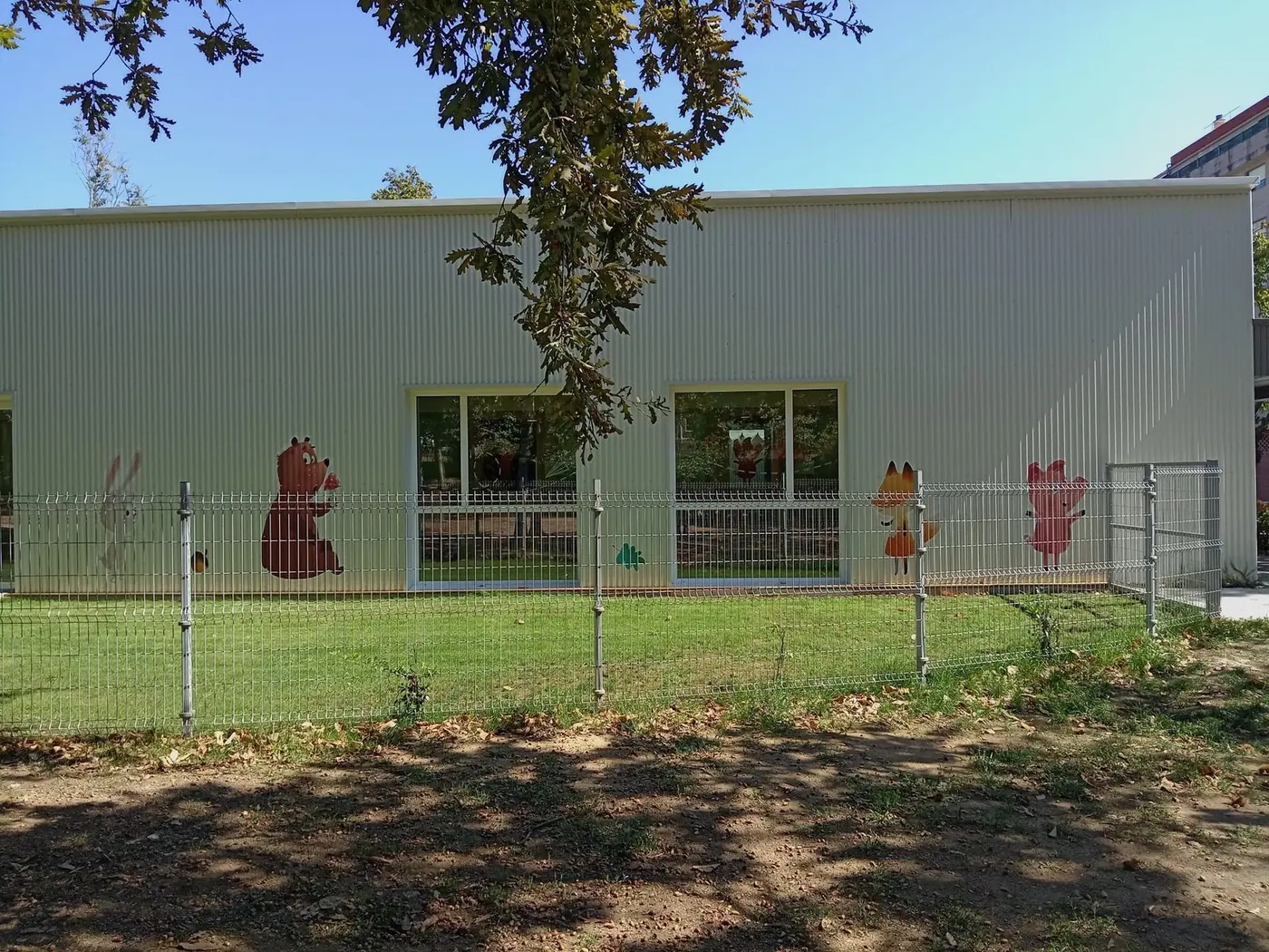 Fachada lateral de la escuela con la valla y los dibujos de animales sobre el muro