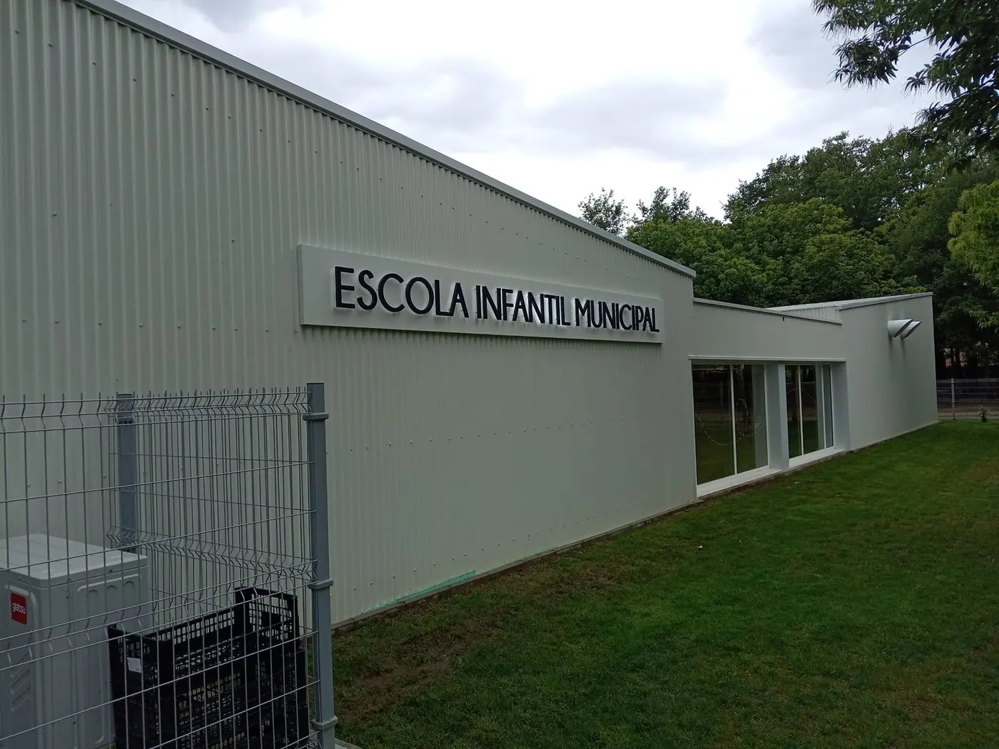 Fachada de la escuela infantil con el rótulo en perspectiva y el césped delante