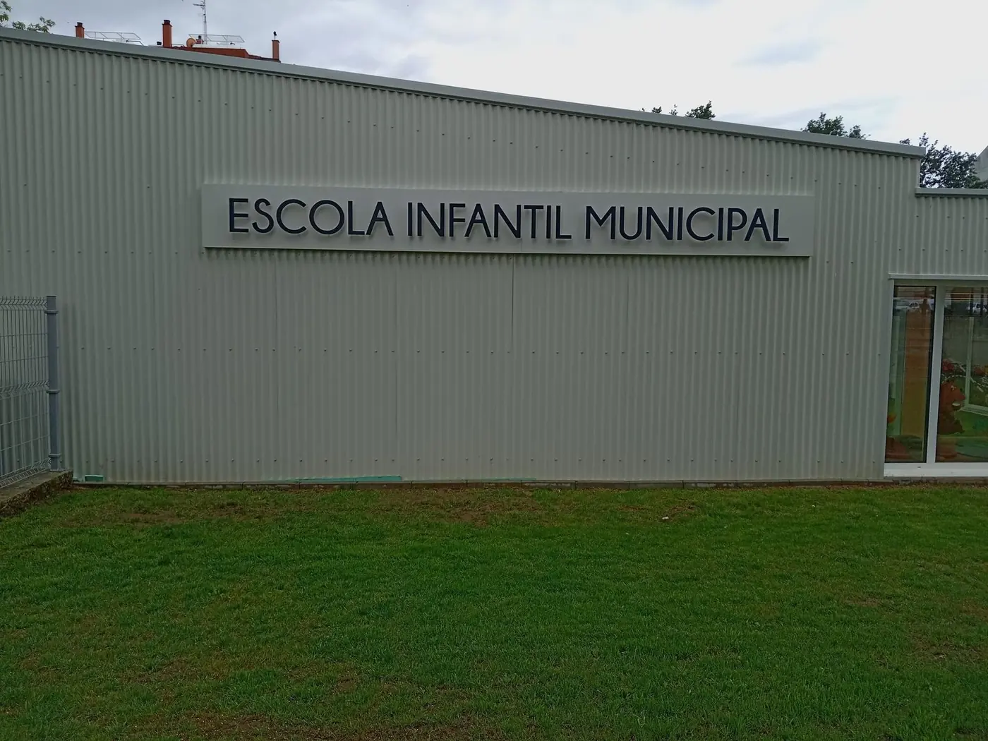Rótulo con letras corpóreas Escola Infantil Municipal sobre la fachada gris
