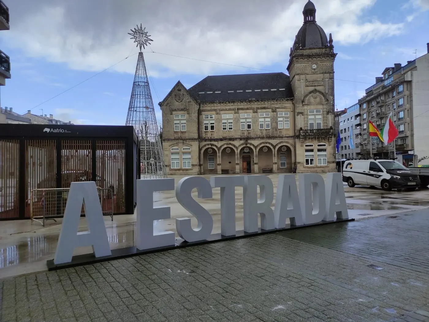 Letras corpóreas gigantes de A Estrada sobre una base en una plaza, con un edificio histórico al fondo