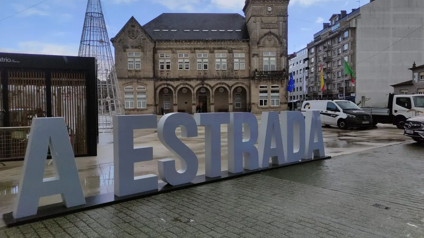 Letras de A Estrada vistas en perspectiva con el edificio de la plaza al fondo