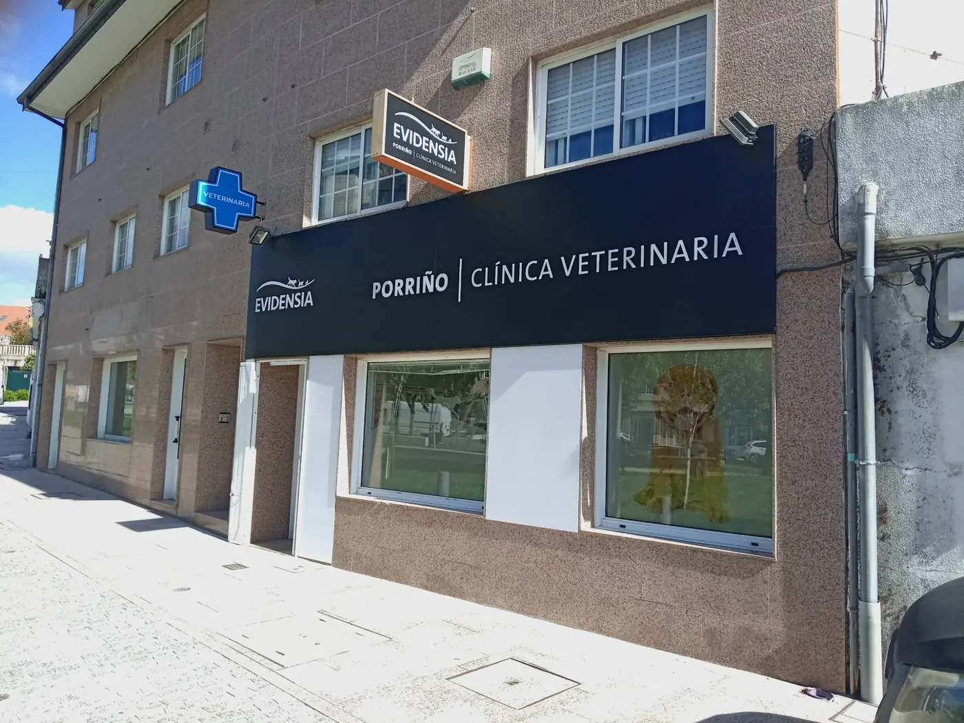 Fachada de la clínica veterinaria Evidensia Porriño con el panel de letras corpóreas, la cruz luminosa y el rótulo en bandera, en perspectiva