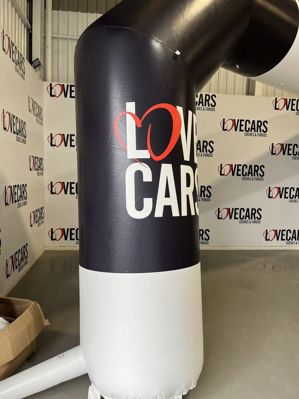 Base blanca y tramo negro de un arco hinchable de Love Cars junto a un photocall de la marca