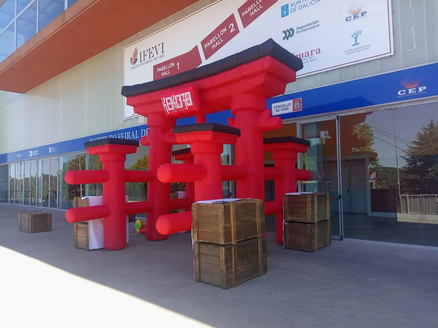 Pórtico hinchable rojo con forma de torii y cajas de madera a la entrada de un recinto ferial