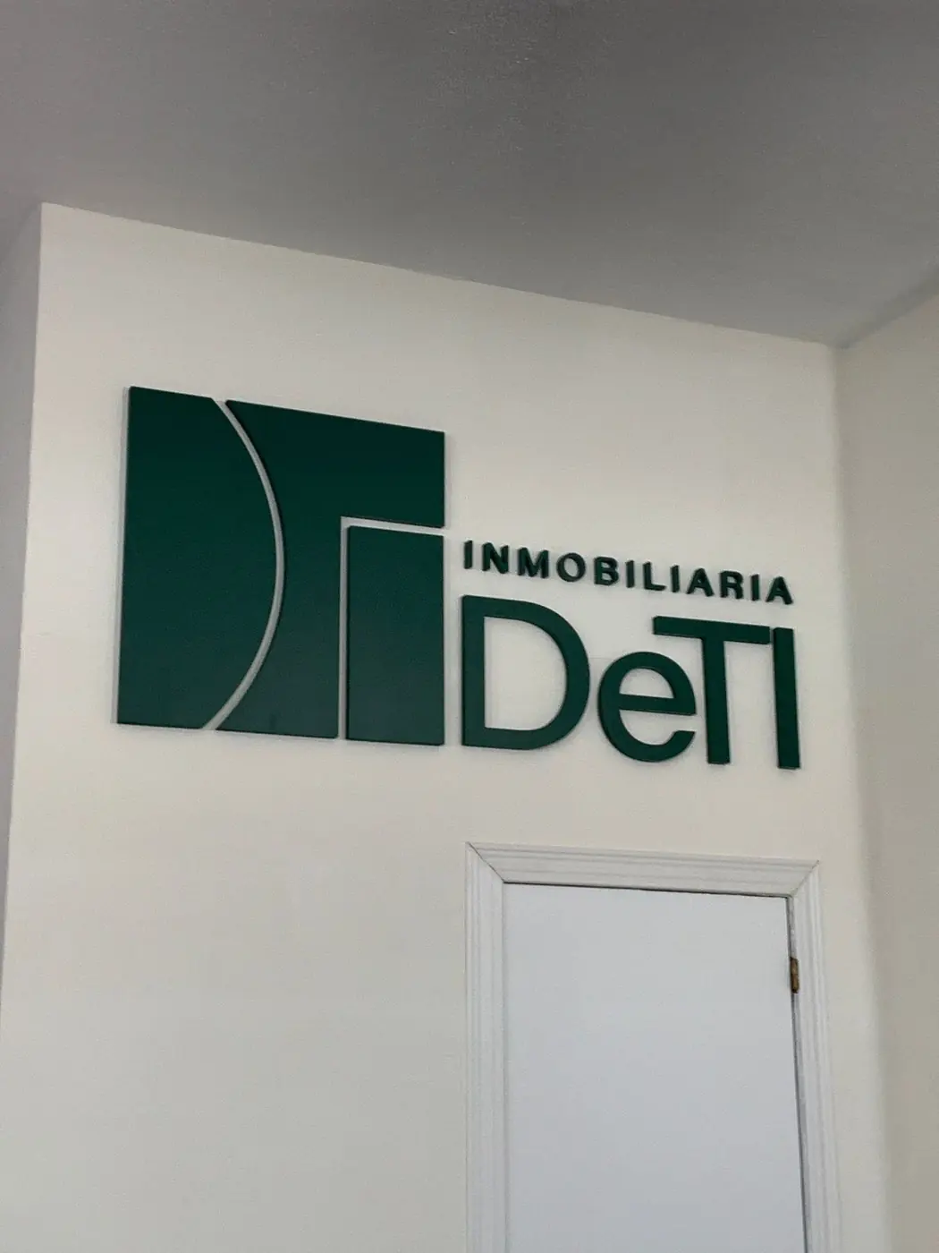 Logotipo corpóreo verde de Inmobiliaria DeTi sobre pared blanca