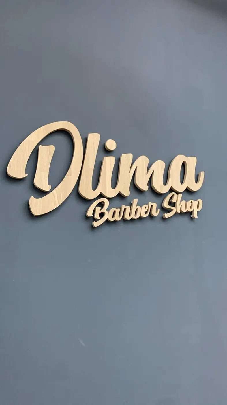 Letras doradas de Dlima Barber Shop sobre pared gris