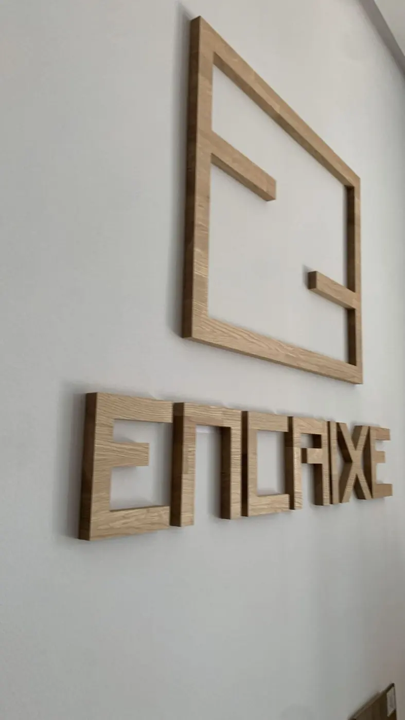 Logotipo corpóreo de Encaixe en madera sobre pared blanca
