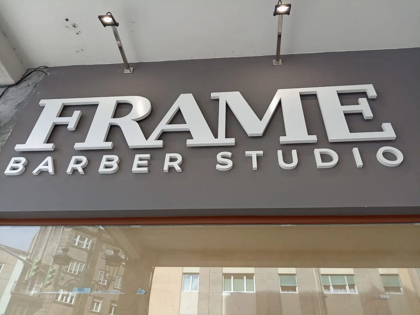 Letras corpóreas blancas de Frame Barber Studio sobre la fachada gris del local