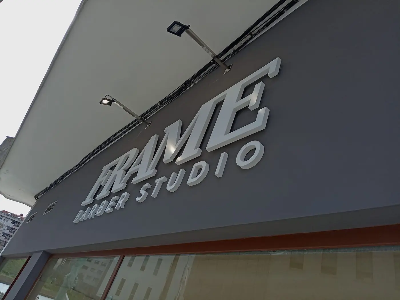 Letras corpóreas de Frame Barber Studio sobre fachada gris, vista en perspectiva