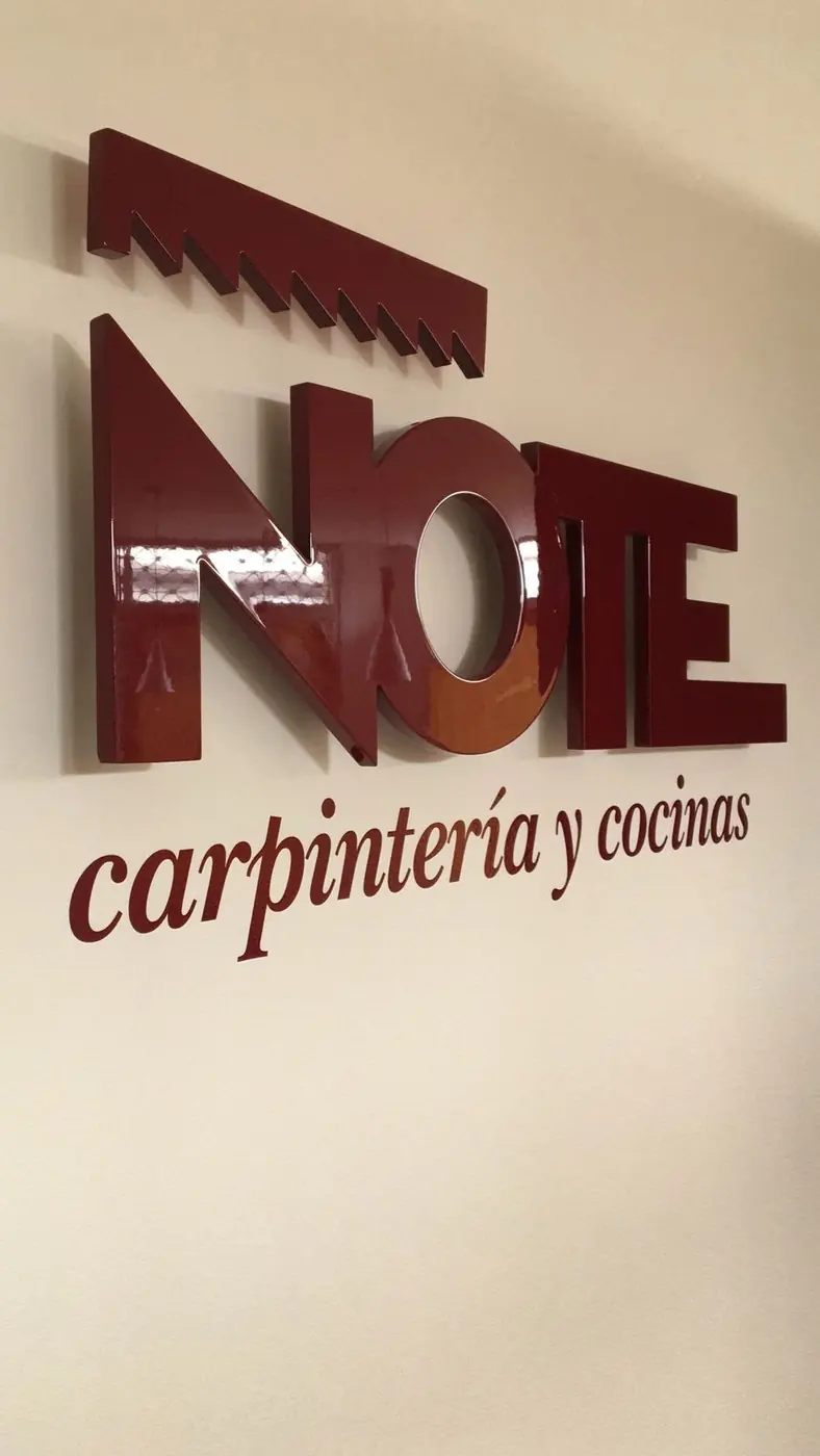 Letras corpóreas granates de Note carpintería y cocinas sobre pared blanca