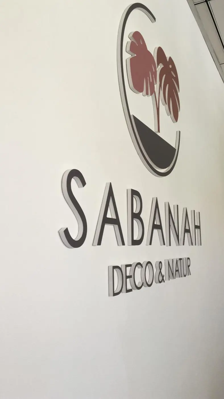 Logotipo de Sabanah Deco & Natur en relieve sobre pared blanca