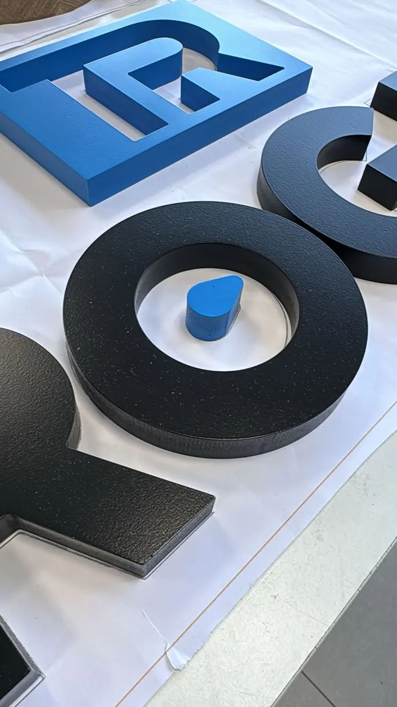 Letras corpóreas en negro y azul en producción sobre la mesa del taller