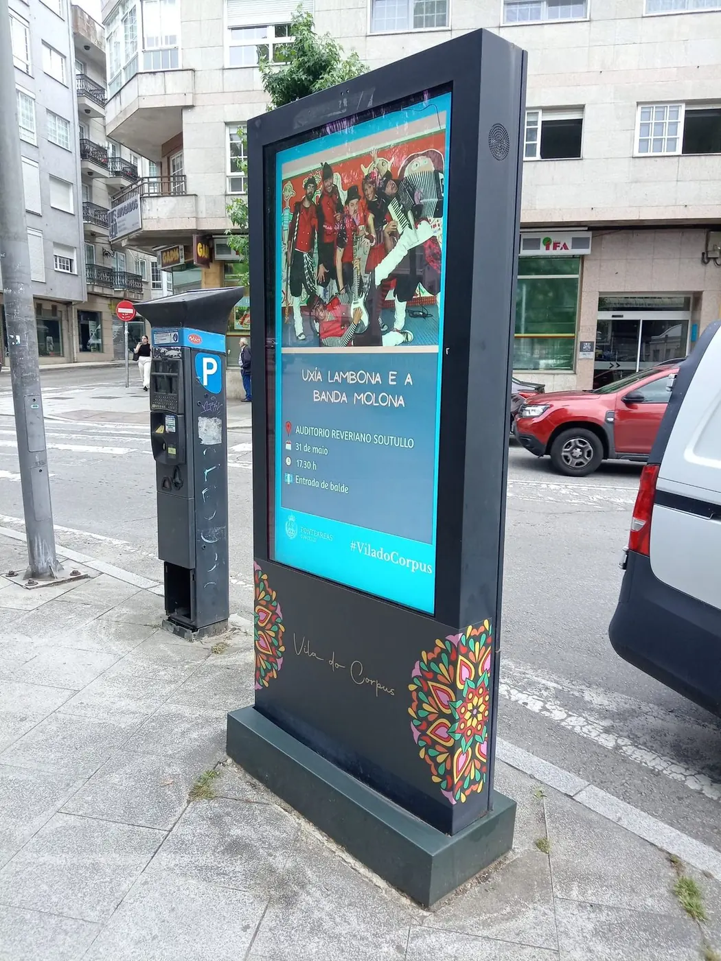 Mupi luminoso con cartelería de fiestas, junto a un parquímetro