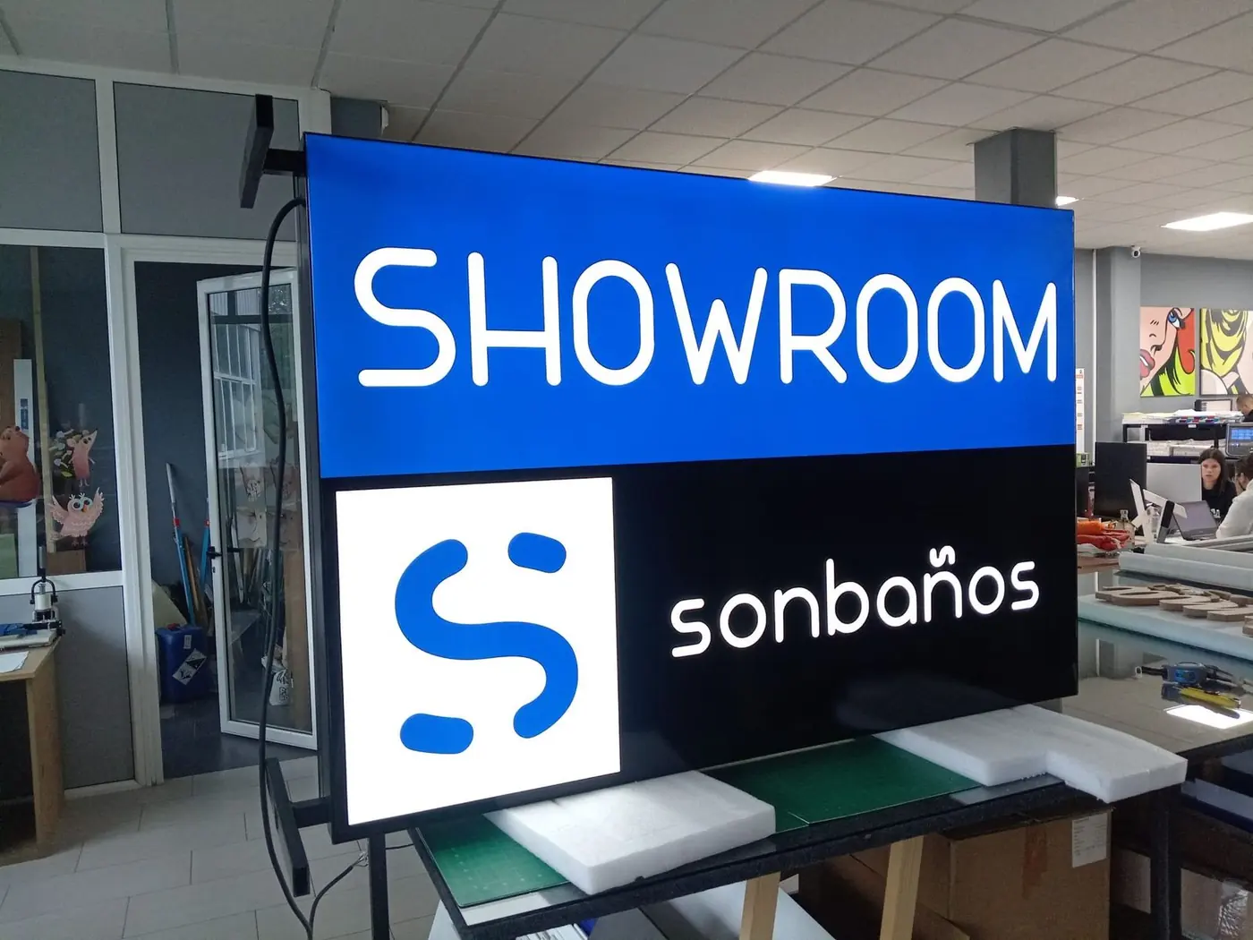 Rótulo luminoso Showroom Sonbaños en el taller, con fondo azul y logotipo retroiluminado