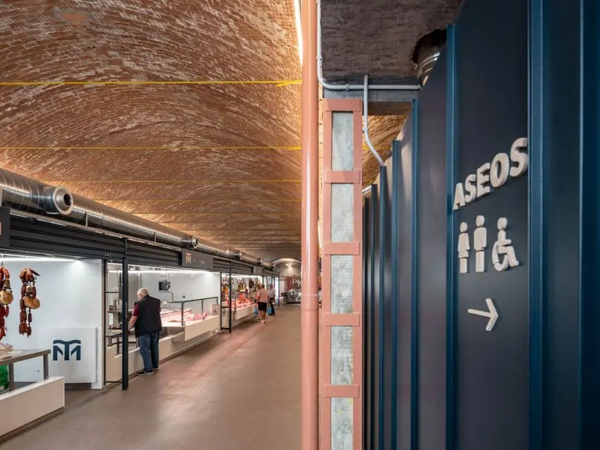 Cartel de aseos con pictogramas y flecha junto al pasillo de puestos