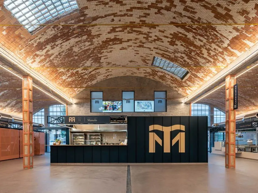 Interior de MercaTea con el gran logotipo dorado sobre el puesto negro bajo la bóveda de ladrillo