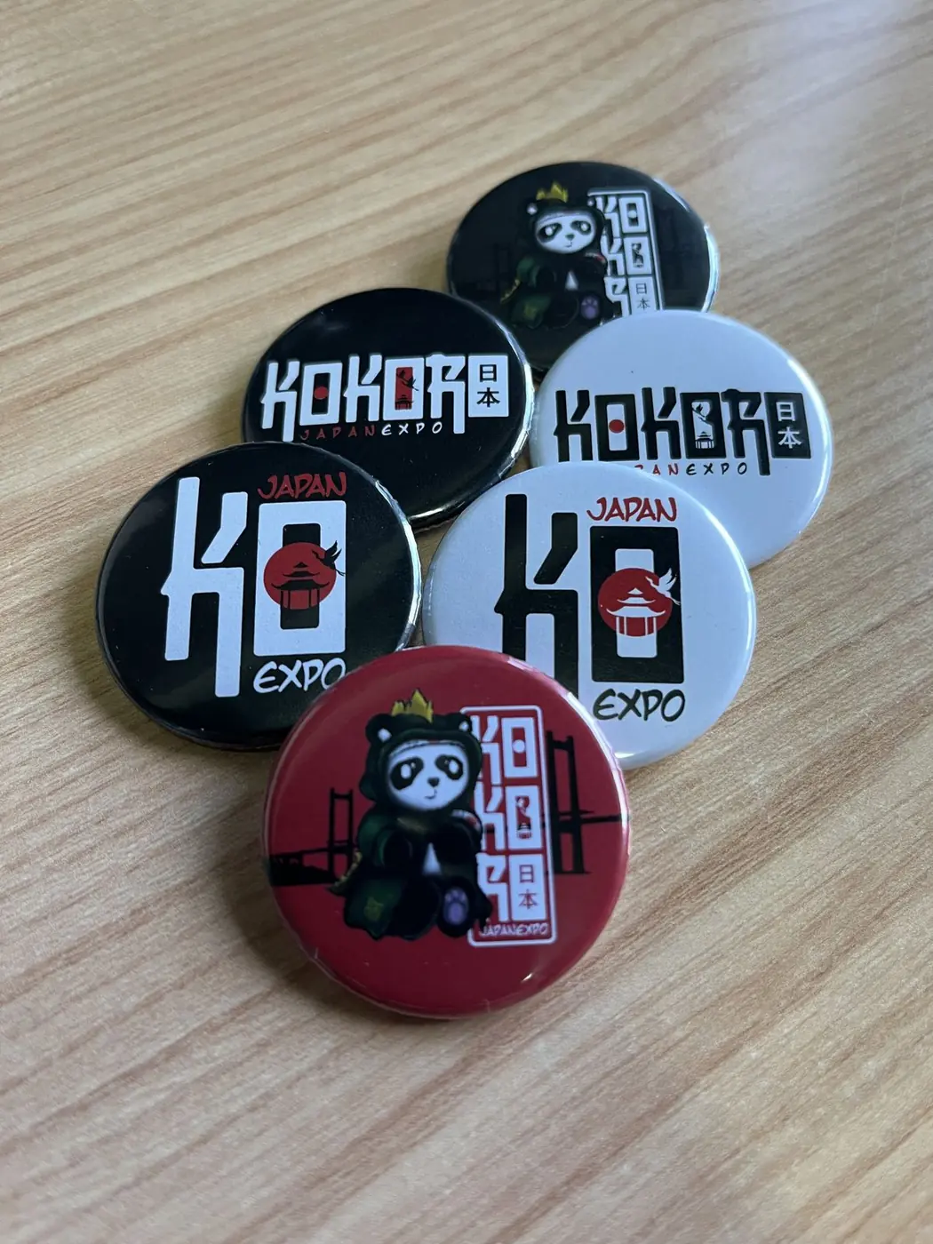 Chapas redondas de Kokoro Expo Japan en negro, blanco y rojo sobre una mesa de madera