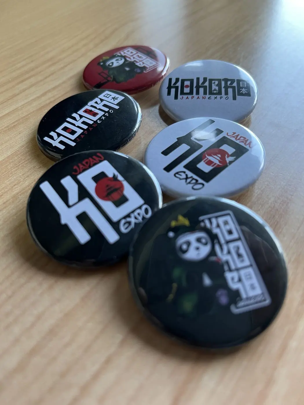 Chapas redondas de Kokoro Expo Japan en negro, blanco y rojo sobre una mesa de madera