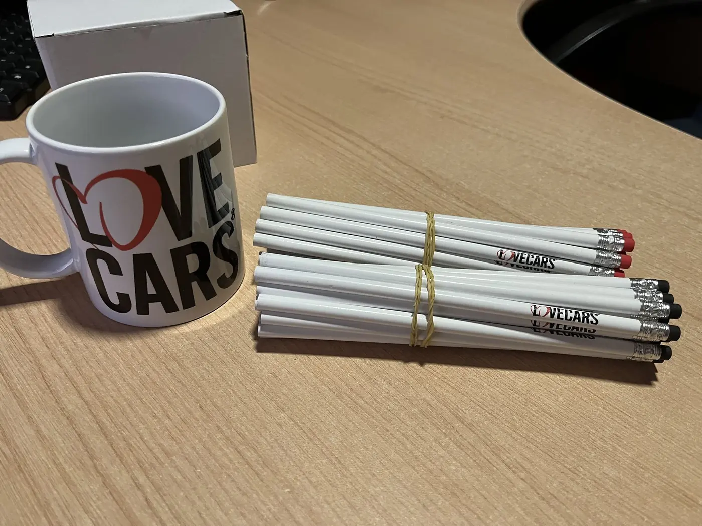 Taza de Love Cars junto a un manojo de lápices blancos personalizados con la marca