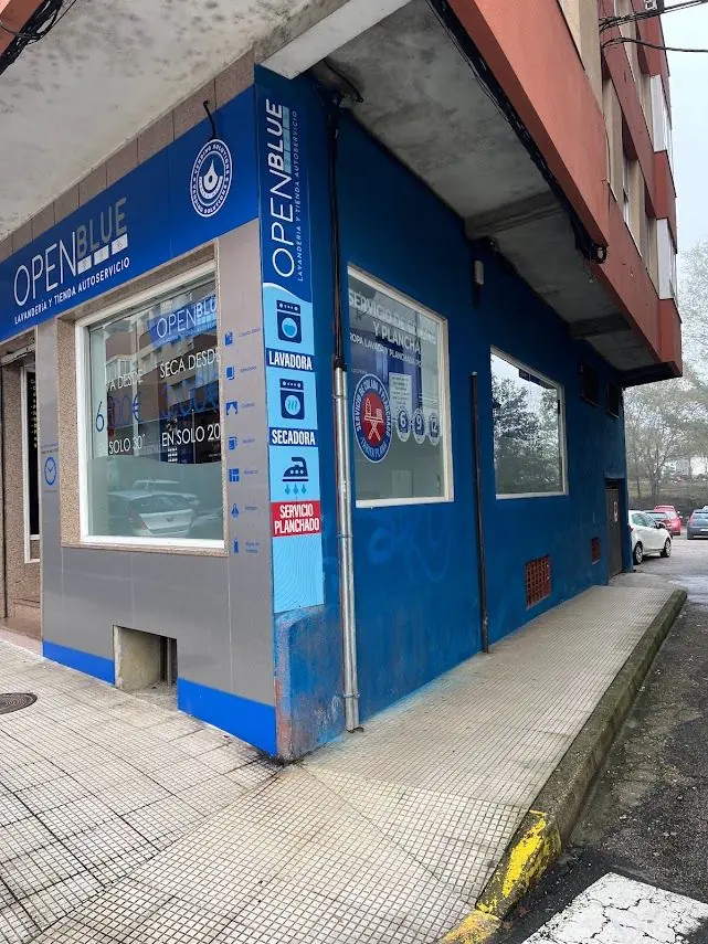 Fachada de la lavandería OpenBlue en esquina, con rótulo y vinilos laterales