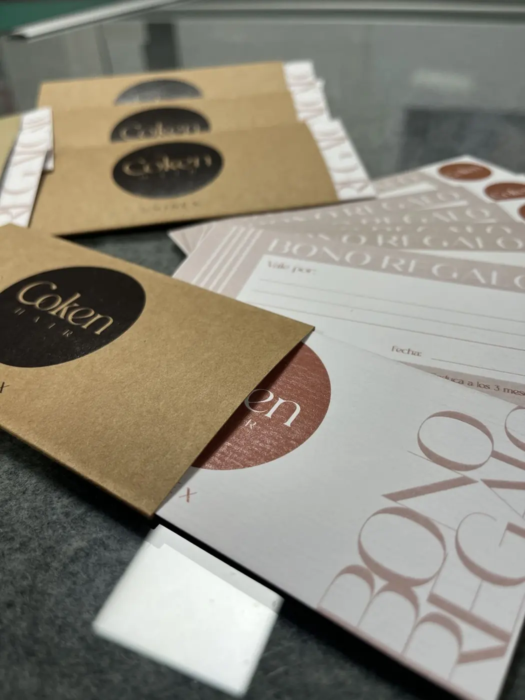Sobres de cartón kraft con pegatina negra de Coken, tarjetas y bono regalo sobre la mesa