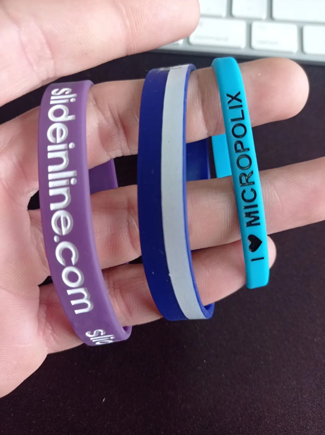 Tres pulseras de silicona personalizadas en morado, azul y turquesa sobre una mano