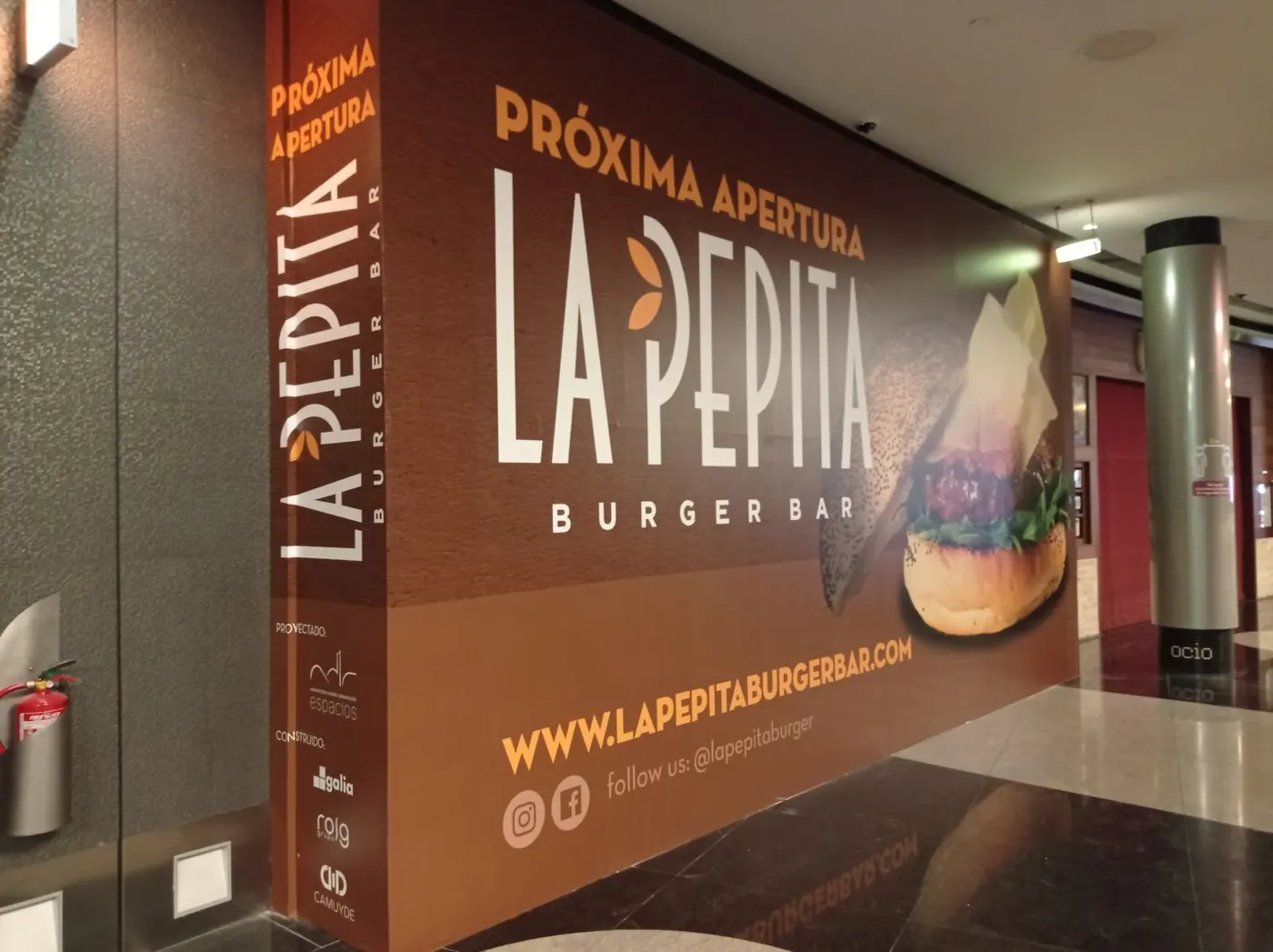 Lona de La Pepita Burger Bar con el texto Próxima apertura y la dirección web, rodeando una columna