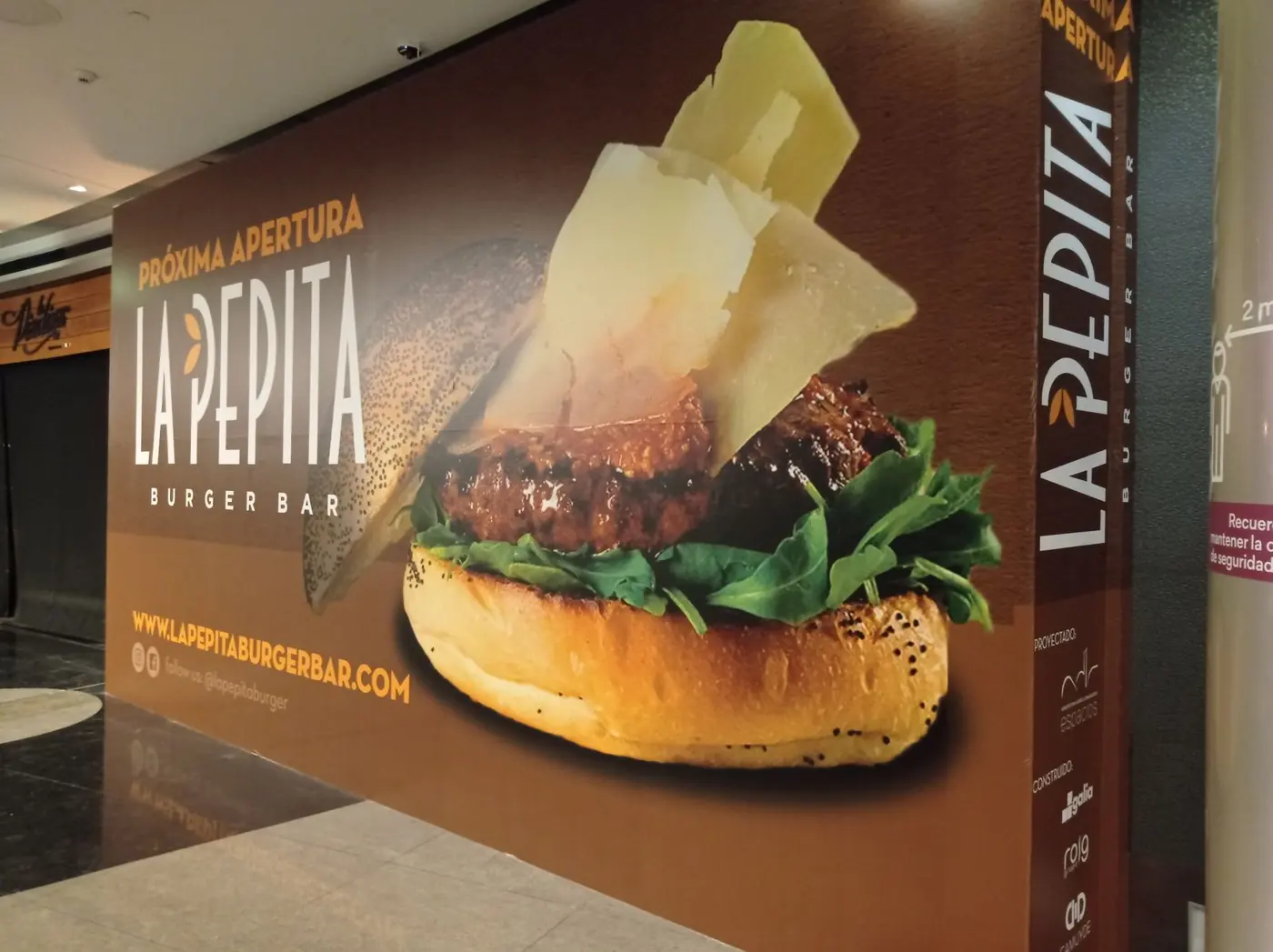 Lona de gran formato de La Pepita con hamburguesa cubriendo la pared de un centro comercial