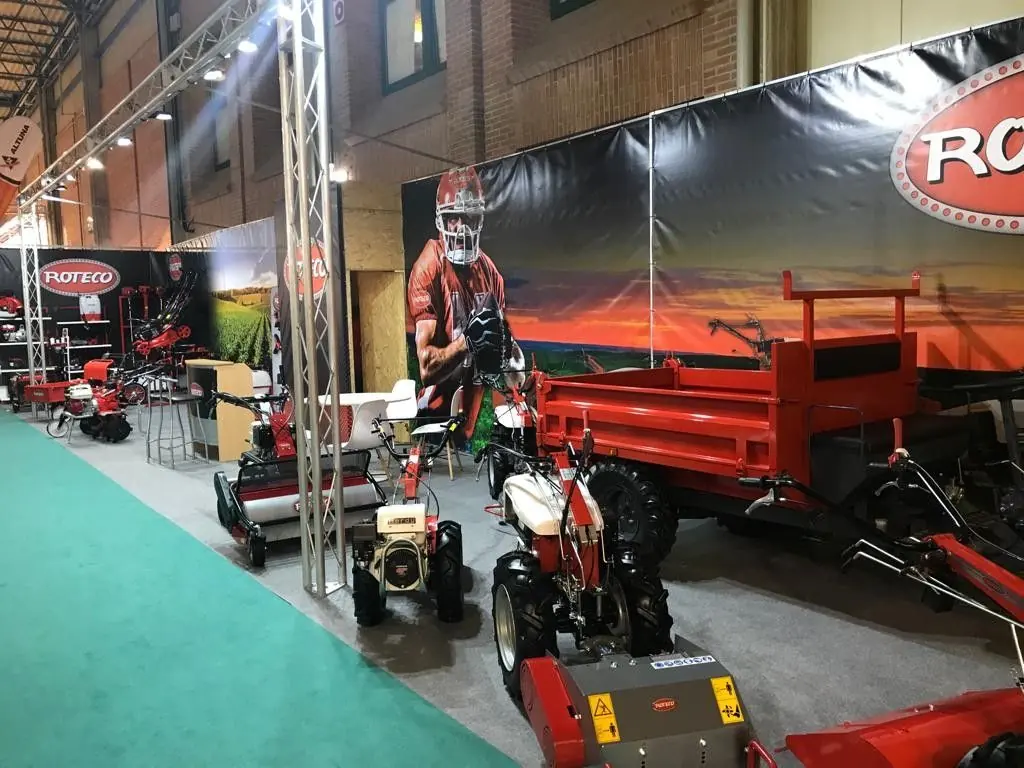Stand de Roteco con fondo impreso de un campo de cultivo y maquinaria expuesta sobre moqueta verde