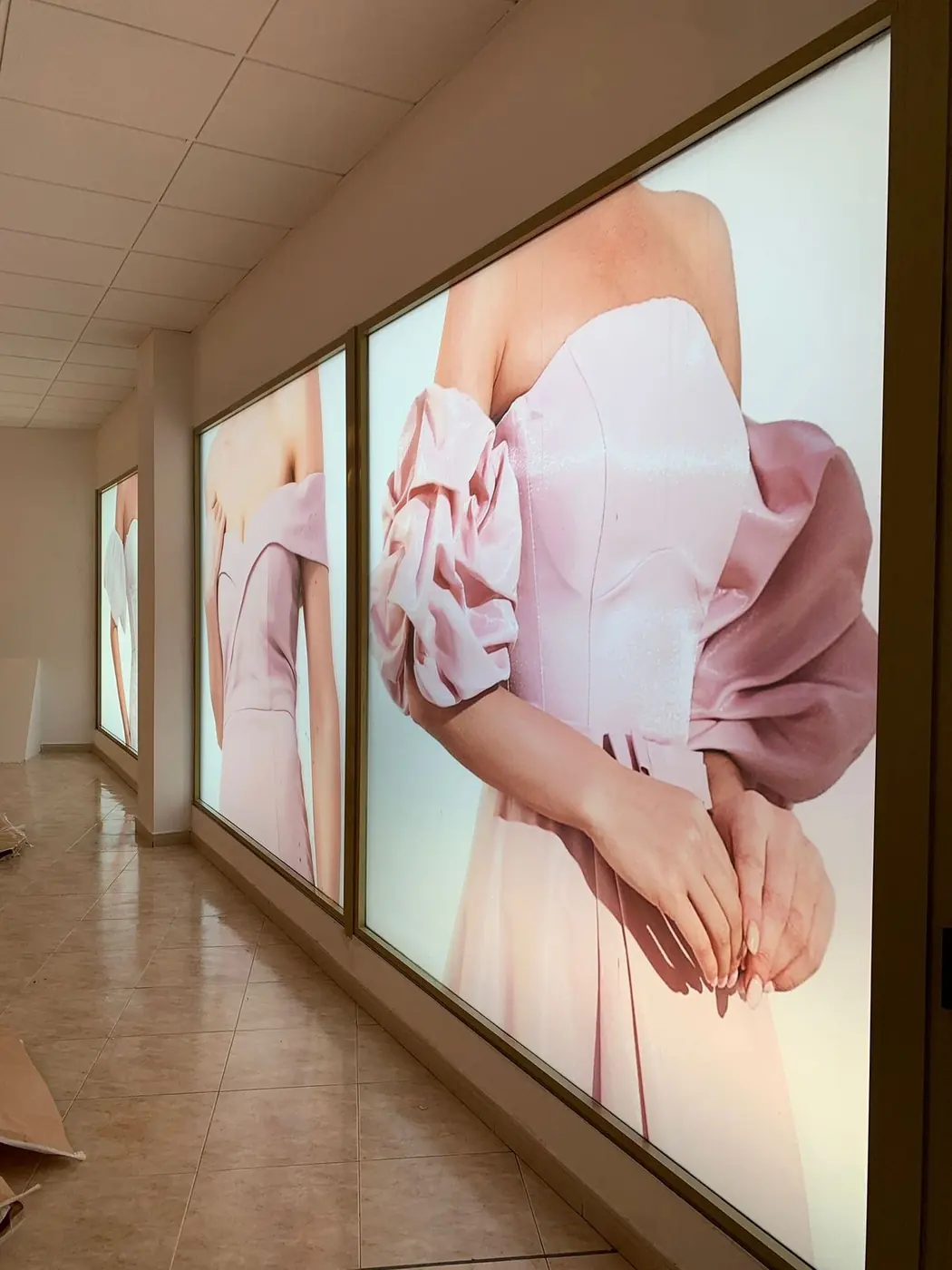 Vinilos retroiluminados con la imagen de un vestido rosa sobre los ventanales de un local