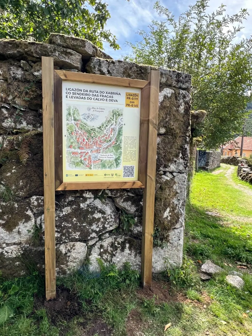Panel con mapa ilustrado de la Franqueira y código QR junto a un muro de piedra